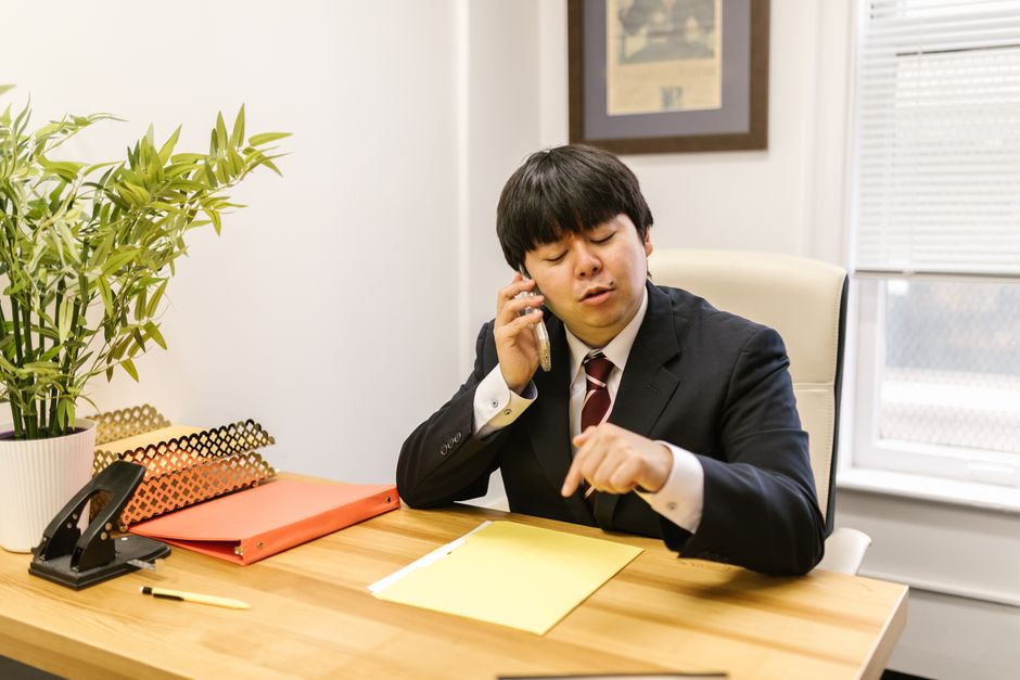 Professional businessman in corporate attire discussing on phone amidst office setting.