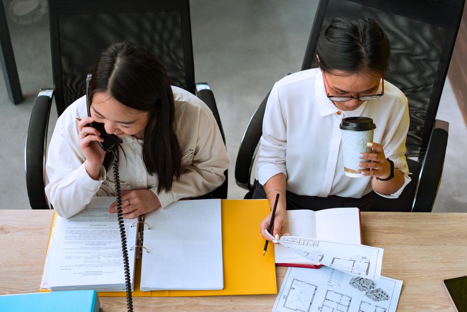 Two women professionals collaborating in a business meeting with documents and phone communication.